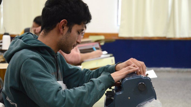 Carlos Tapia en el aula de la facultad con su vieja máquina que escribe en braille y con su nueva notebook.