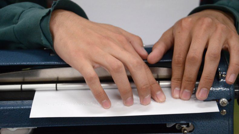 Carlos Tapia en el aula de la facultad con su vieja máquina que escribe en braille y con su nueva notebook.