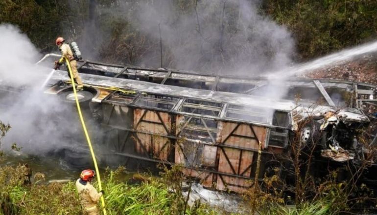 Bomberos trabajan entre humo y restos del colectivo incendiado tras el accidente en una zona de difícil acceso en Ecuador.