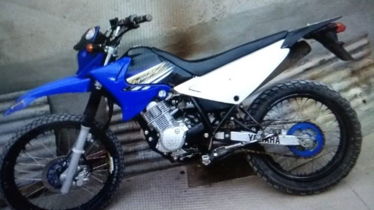 La moto es azul y blanca y no tiene la patente a la vista.