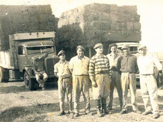 Camiones con fardos listos para partir para la capital, los camioneros Mangas y Pirronito, los changarines y Adolfo Grobocopatel en el centro, con botas y boina. El destino final era Dorso Hnos., en Lomas de Zamora, y Cortés y Magliani de Lanús, que luego los distribuirían a los soderos de la zona. Foto: Los Grobo 25 años imaginando y construyendo el futuro.
