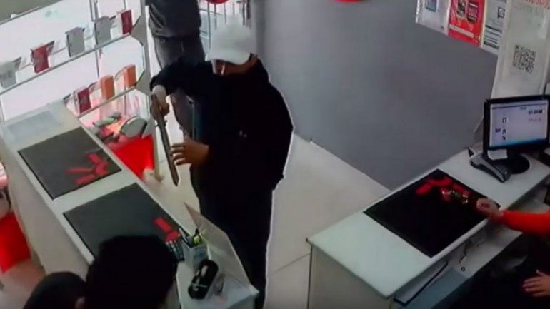 Uno de los delincuentes apunta con una tumbera al empleado.