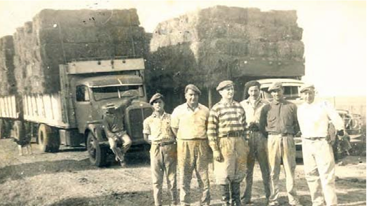 Camiones con fardos listos para partir para la capital, los camioneros Mangas y Pirronito, los changarines y Adolfo Grobocopatel en el centro, con botas y boina. El destino final era Dorso Hnos., en Lomas de Zamora, y Cortés y Magliani de Lanús, que luego los distribuirían a los soderos de la zona. Foto: Los Grobo 25 años imaginando y construyendo el futuro.